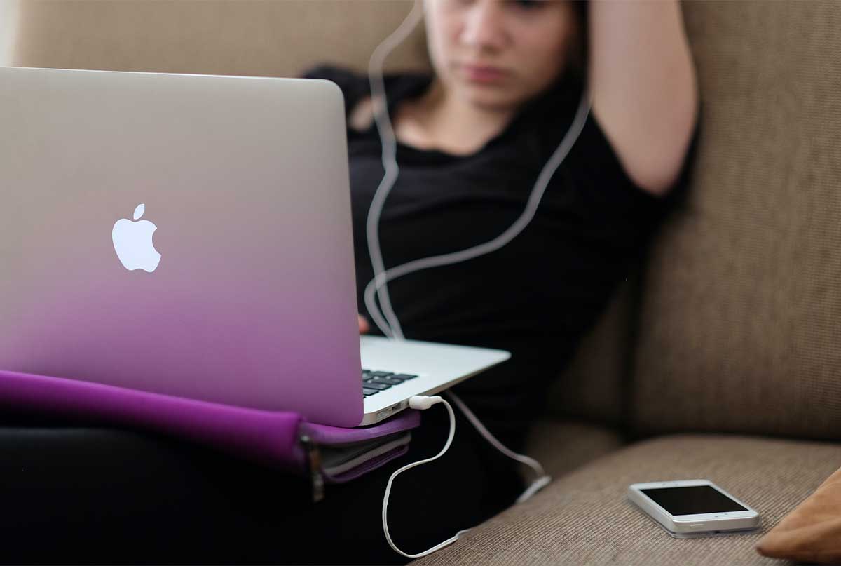 نوجوان دختری که روی مبل نشسته و لپ تاپ رو پاش بازه و گوشی کنارشه