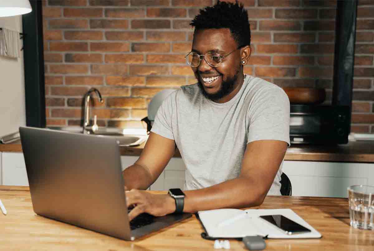اقای سیاهپوست با خنده داره با لپ تاپ کار میکنه و پشتش دیوار اجریه