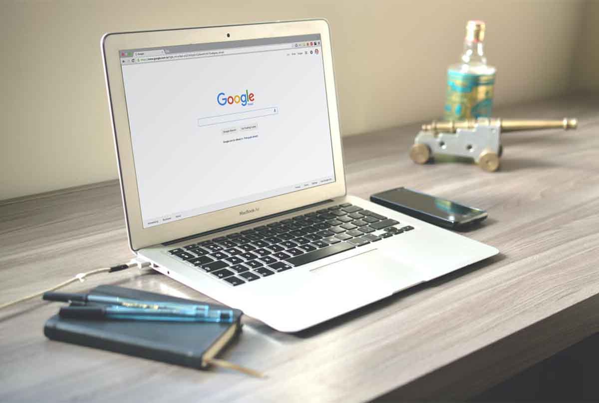 لپ تاپ بازی که صفحه گوگل را نشان میدهد با موبایل و دفتر و خودکار رو میز
