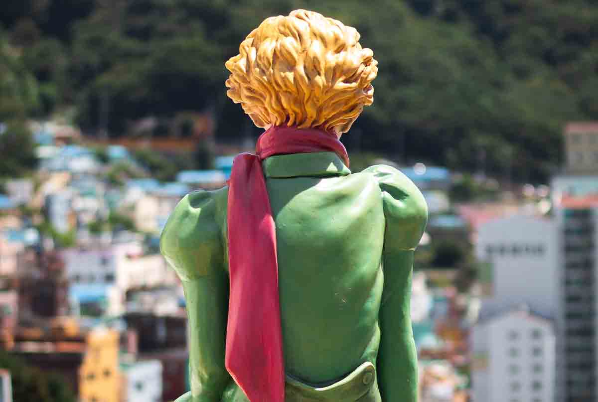 مجسمه شاهزاده کوچولو با موی طلایی و لباس سبز و شال قرمز که پشتش به عکسه