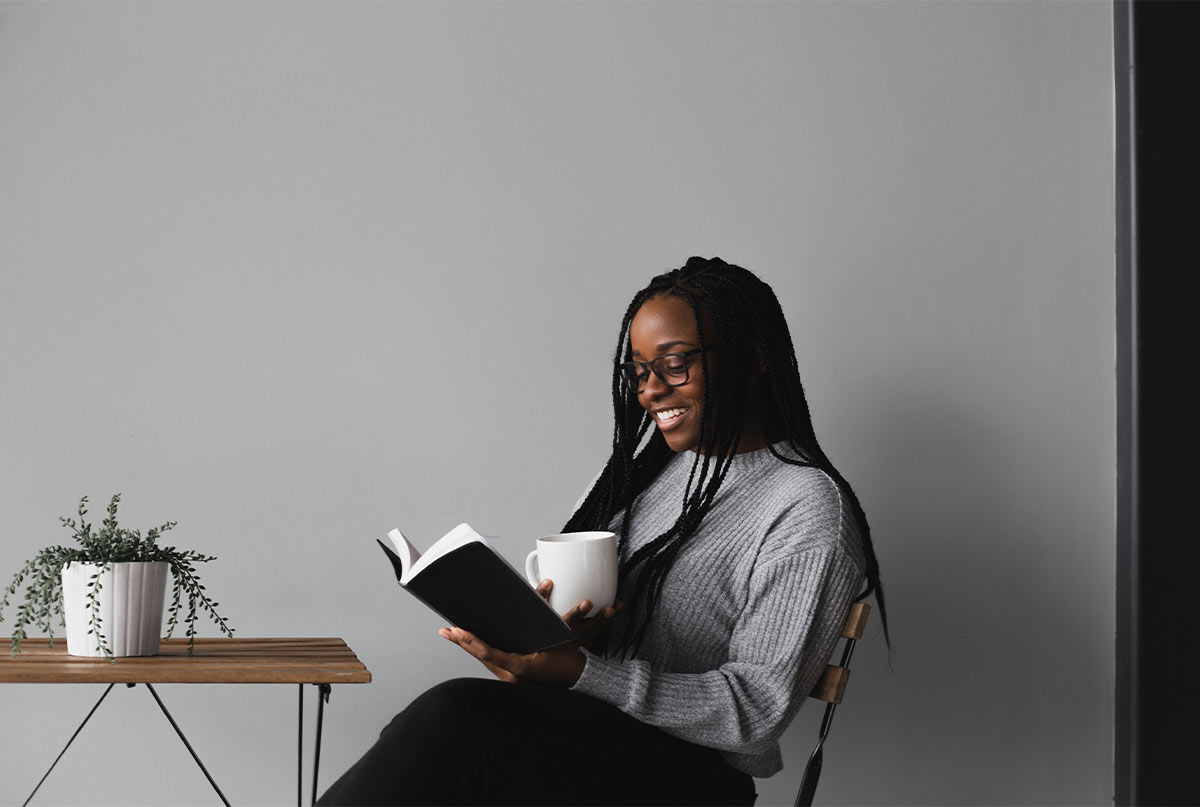 خانم سیاهپوست در حال خواندن کتاب که جلوش رو میز گلدون هست