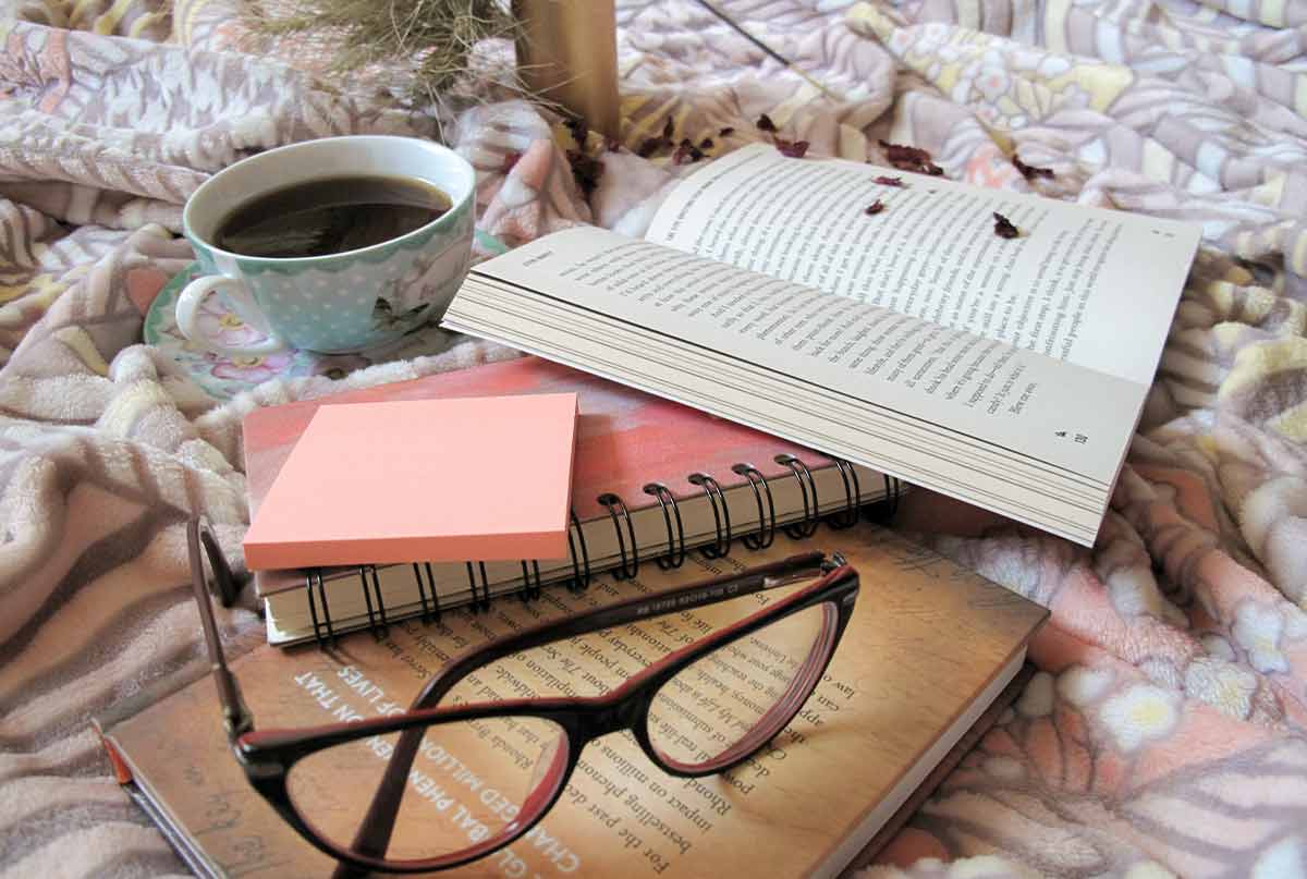 عینک و کتاب و فنجان چای روی زیرانداز خوشگل