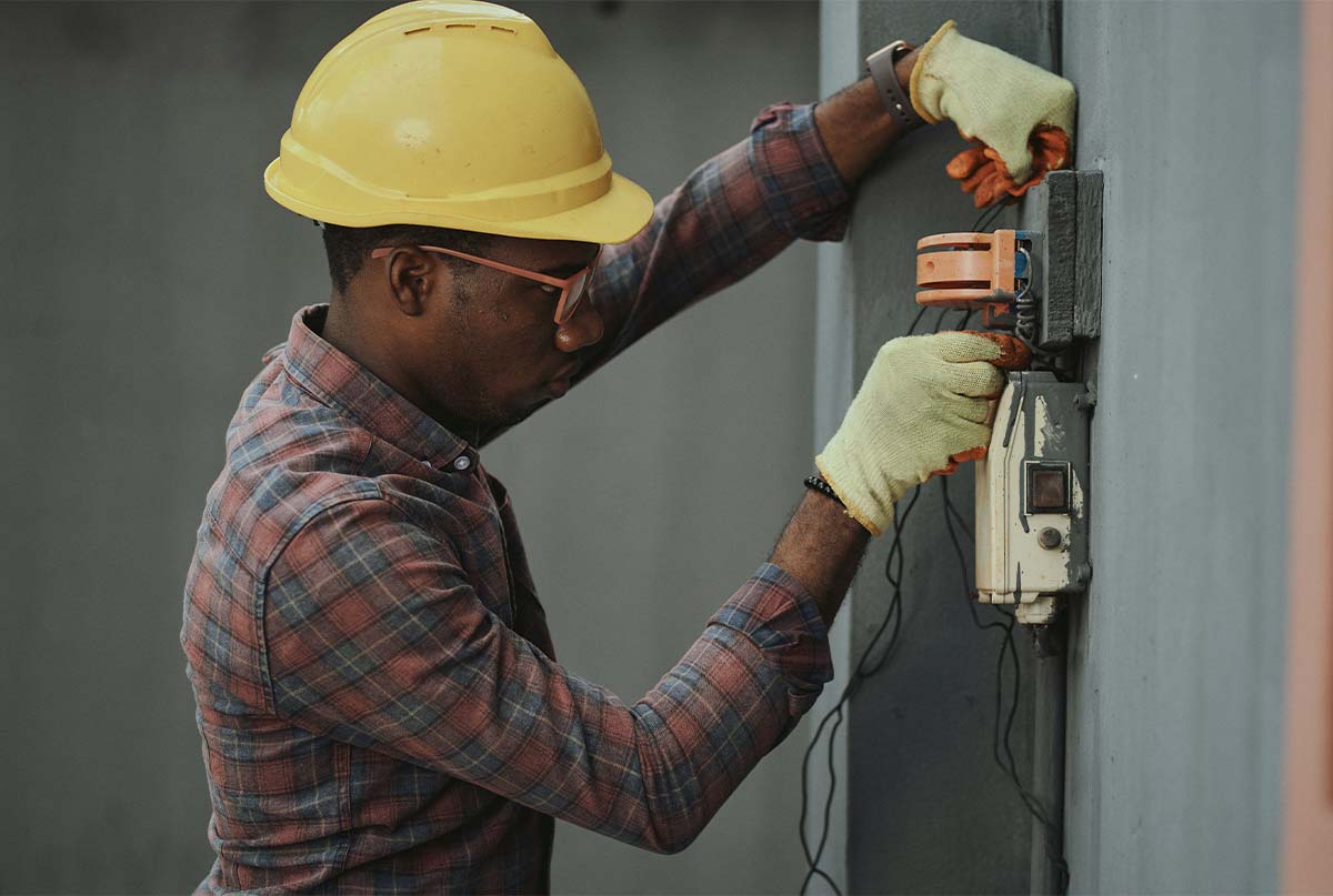 اقای سیاه پوست برق کار در حال انجام کار فنی که کلاه ایمنی سرشه