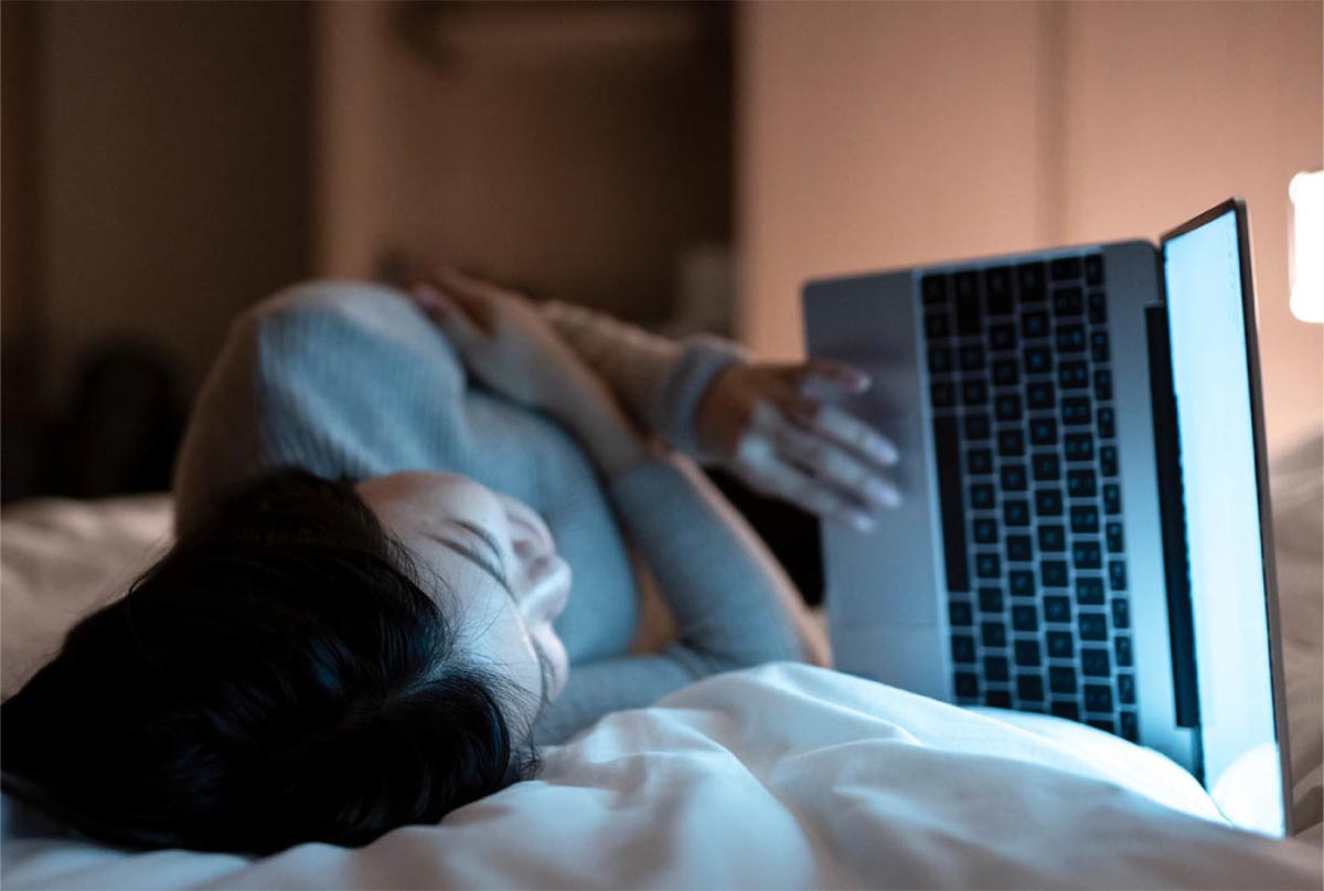 خانمی که رو تخت دراز کشیده و با لپ تاپ کار میکنه