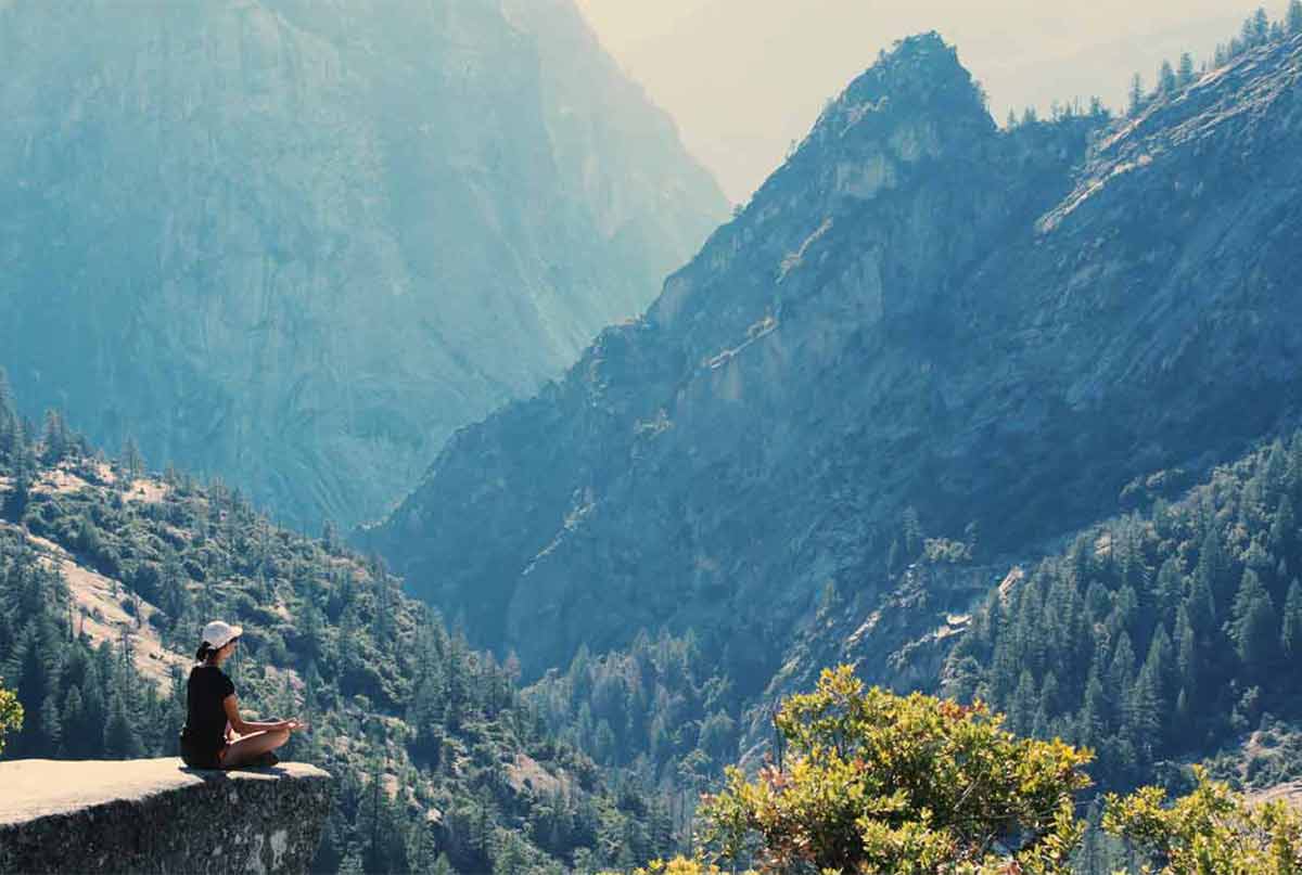 فردی که رو صخره در طبیعتی زیبا رو به کوه های بلند نشسته